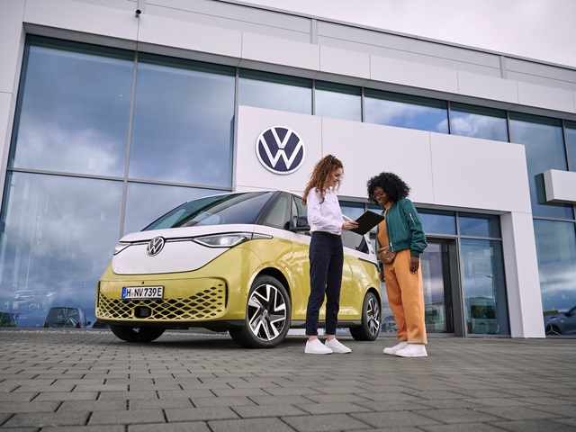 Zwei Personen bei Fahrzeugübergabe vor einem gelben Volkswagen ID. Buzz